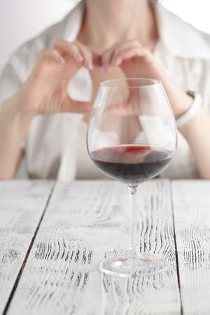 Love to wine. Female hold hands in heart sign against wine glassの写真素材