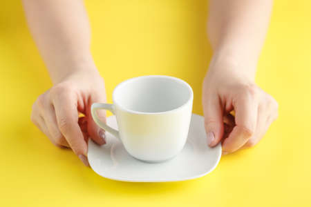 woman hand holding empty white cup on bright yellowの写真素材