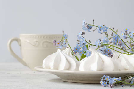 White marshmallows and lilac forget-me-not flowers with green leaves on a white background.の写真素材