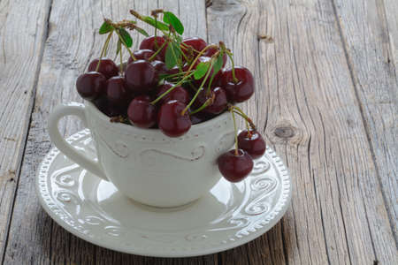 White mug with ripe cherries on old wood backgroundの写真素材