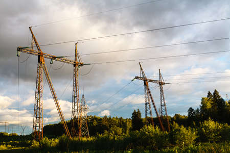high voltage power pylons against blue sky and sun raysの写真素材