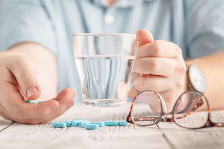 Elderly hand is holding blue tablets with white backgroundの写真素材