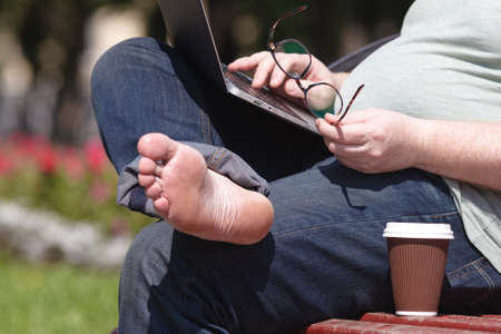 Man sitting on park bench using laptop on a sunny day