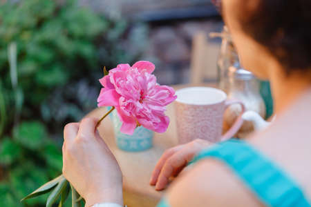 Woman sitting drinking tea at a cafe with flower in handの写真素材