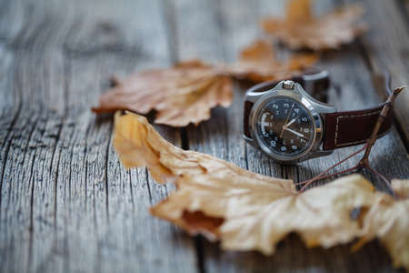 Wrist watch on wooden table with fall leafの写真素材