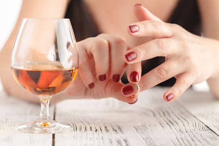 Woman take off wedding ring and drink whiskey on wooden tableの写真素材
