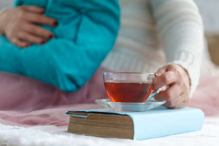 Close up of woman's hands holding a cup of tea, wearing a white sweater and enjoying the leisure timeの写真素材