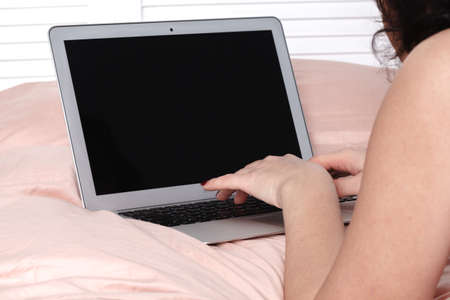 Beautiful lady busy early in the morning working from bedの写真素材