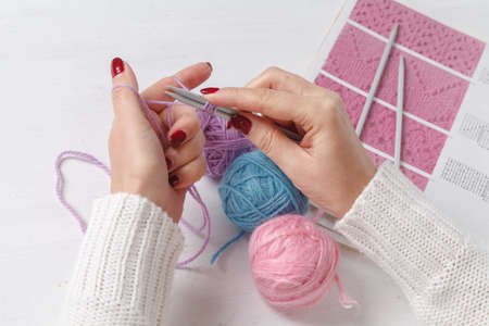 Caucasian woman knits woolen clothes. Holding knitting needles at hands
