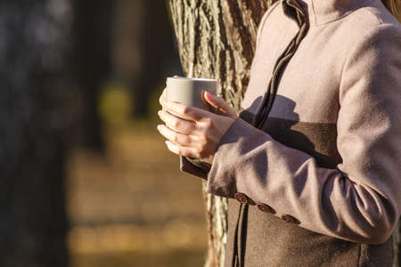 holding coffee or tea from cup in autumn parkの写真素材