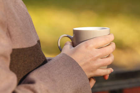 Close up of woman drinking from a cup against autumn leaves patternの写真素材