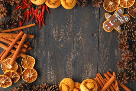 Traditional Xmas frame with spices, speculoos biscuits, star cookies and assorted nuts decorated with dried orange around central copyspace on a rustic wood backgroundの写真素材
