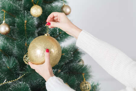 X-mas, winter holidays and people concept - happy young woman decorating christmas tree with ball at homeの写真素材