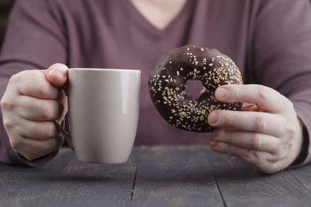 man holding glazed donut and cup of coffeeの写真素材