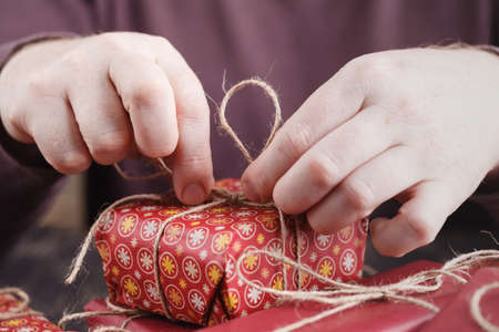 Male hands wrap Christmas gift on wooden table.の写真素材