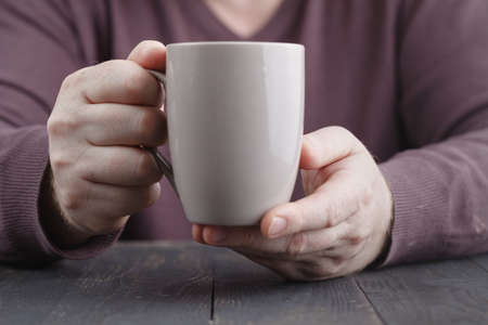 Man holding in hands cup of coffee on wooden backgroundの写真素材