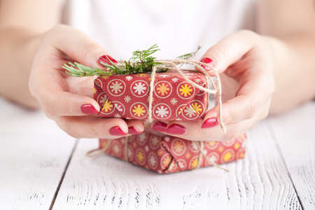 Close up of female hands holding a small christmas gift wrapped with twine. Small gift in the hands of a woman indoor. Shallow depth of field with focus on the little boxの写真素材