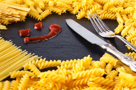 Frame of uncooked pasta on slate with ketchup