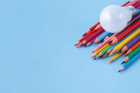 Heap of colour pencils and light bulb on blue background