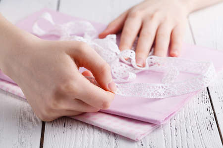 Making table decorations. A shot of woman sewing a natural beige linen tablecloth, towels and napkins with rose print and a crochet white linen lace trim, using needlesの写真素材