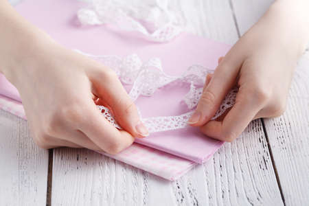 Making table decorations. A shot of woman sewing a natural beige linen tablecloth, towels and napkins with rose print and a crochet white linen lace trim, using needlesの写真素材