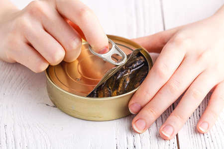 Open fish can with hands and fork on table