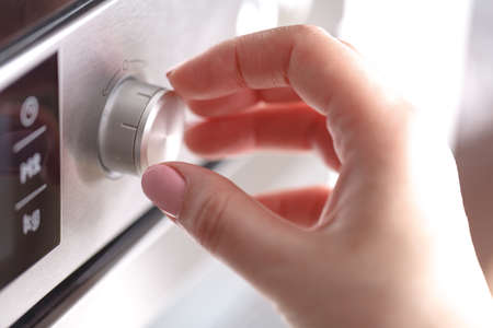 Hand holding rotate dial circle button heat of microwave oven for cooking food in kitchen room at...