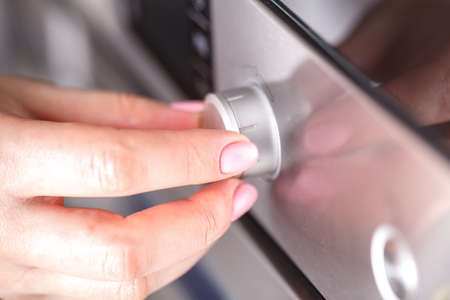Hand holding rotate dial circle button heat of microwave oven for cooking food in kitchen room at...