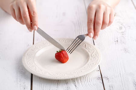 Female eat one fresh strawberry with forkの写真素材