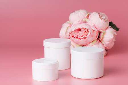 Cosmetic cream container and pink flowers on pink plaint  background