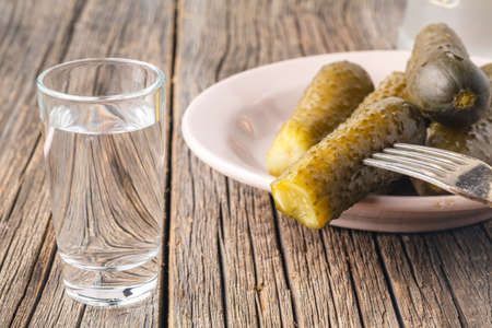 Russian style.Shot glasses of vodka  and pickled cucumbers . On a black rustic wooden backgroundの写真素材