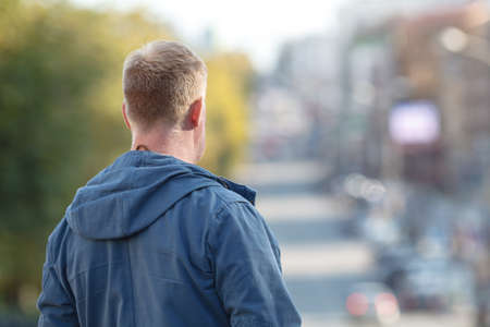 man wearing a jacket standing high up on a mountain with a cityscape behind him on a cold autumn day