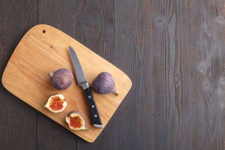 Juicy fresh whole fig fruits and one cut figs on wooden cutting board on dark backgroundの写真素材
