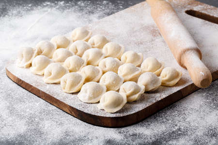 Uncooked russian pelmeni on cutting board and ingredients for homemade pelmeni on white table. Process of making pelmeni, ravioli or dumplings with meatの写真素材