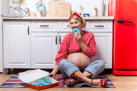 pregnant woman with belly holding donut. The concept weight control and an unhealthy diet during pregnancyの写真素材