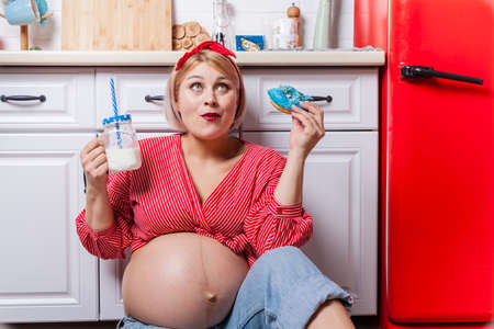 pregnant woman with belly holding donut. The concept weight control and an unhealthy diet during pregnancyの写真素材