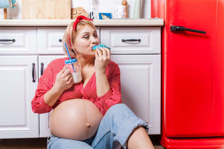 Pregnancy and unhealthy eating concept: pregnant woman eats a tasty doughnutの写真素材
