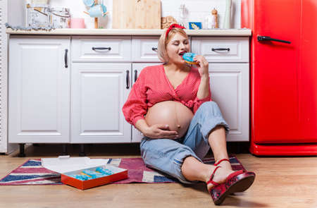 Pregnancy and unhealthy eating concept: pregnant woman holds a tasty doughnuts in her handの写真素材