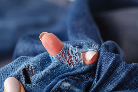 Hole and Threads on Denim Jeans. Ripped Destroyed Torn Blue jeans background. Close up blue jean textureの写真素材
