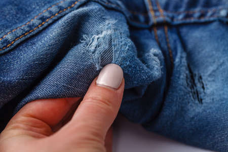 Hole and Threads on Denim Jeans. Ripped Destroyed Torn Blue jeans background. Close up blue jean textureの写真素材