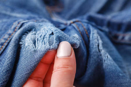 Hole and Threads on Denim Jeans. Ripped Destroyed Torn Blue jeans background. Close up blue jean textureの写真素材