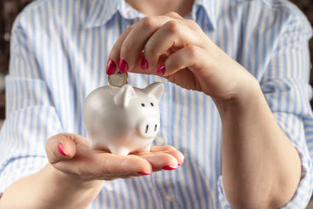savings concept,white piggy bank with human female hand inserting  coin insideの写真素材