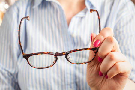 close up spectacles with girl hand holding glasses on wood desk. Release concept. spectacles selective focus.の写真素材