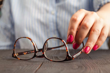 close up spectacles with girl hand holding glasses on wood desk. Release concept. spectacles selective focus.の写真素材