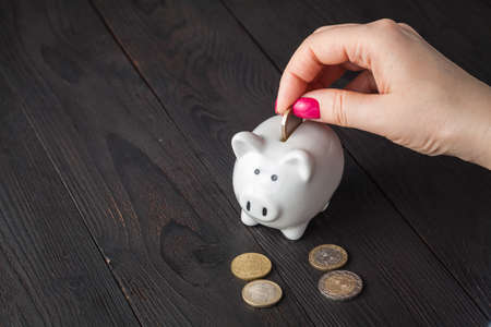 savings, money, annuity insurance, retirement and people concept - close up of woman hand putting coin into piggy bankの写真素材