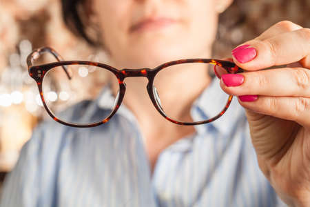 female hand holding a brown framed glassesの写真素材