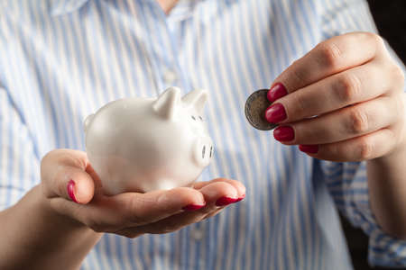 Female hand putting coin into piggy bank closeupの写真素材
