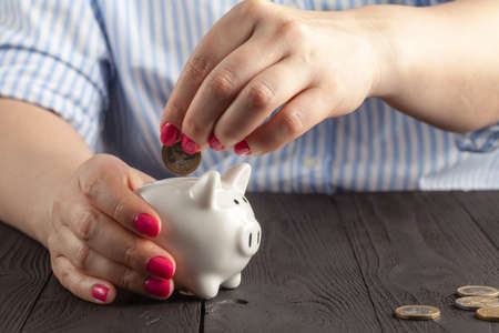 savings concept,white piggy bank with human female hand inserting  coin insideの写真素材