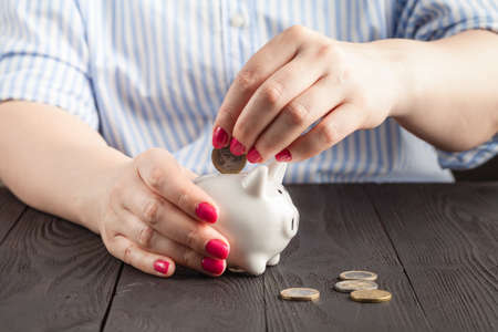 Close-Up Woman Hand is Putting a Money Coin into Piggy Bank on tableの写真素材