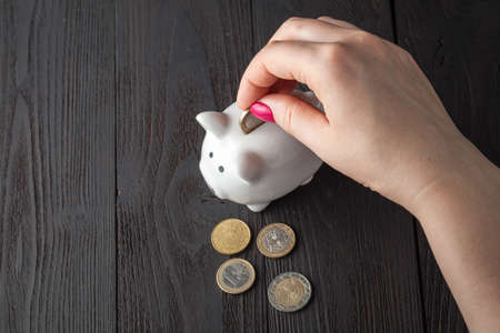 savings concept,white piggy bank with human female hand inserting  coin insideの写真素材